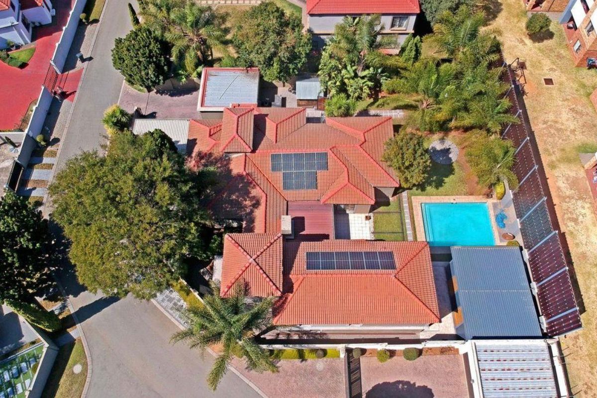 Aerial view of the property showcasing the tiled roof with integrated solar panels, a private swimming pool, and established garden areas.