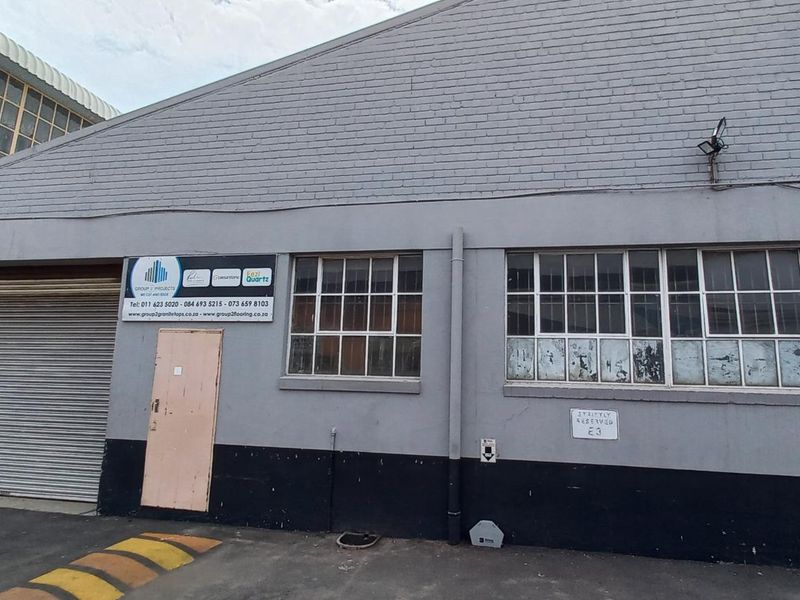 Front elevation of an industrial warehouse featuring a roller shutter door, multi-pane windows, and a painted brick facade.