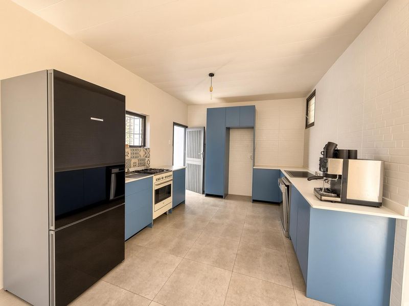 Modern kitchen featuring blue cabinetry, tiled backsplash, gas stove, oven, and neutral floor tiles, offering a clean and functional workspace.