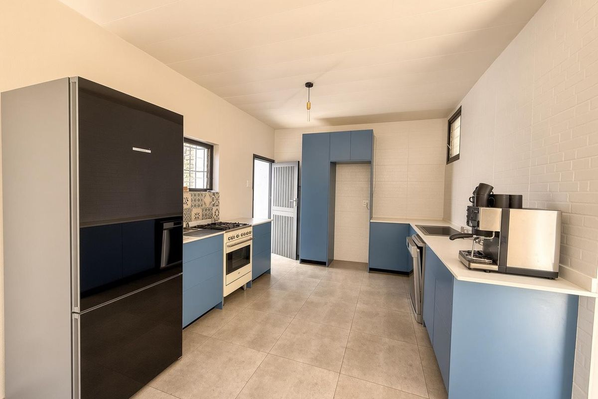 Modern kitchen featuring blue cabinetry, tiled backsplash, gas stove, oven, and neutral floor tiles, offering a clean and functional workspace.