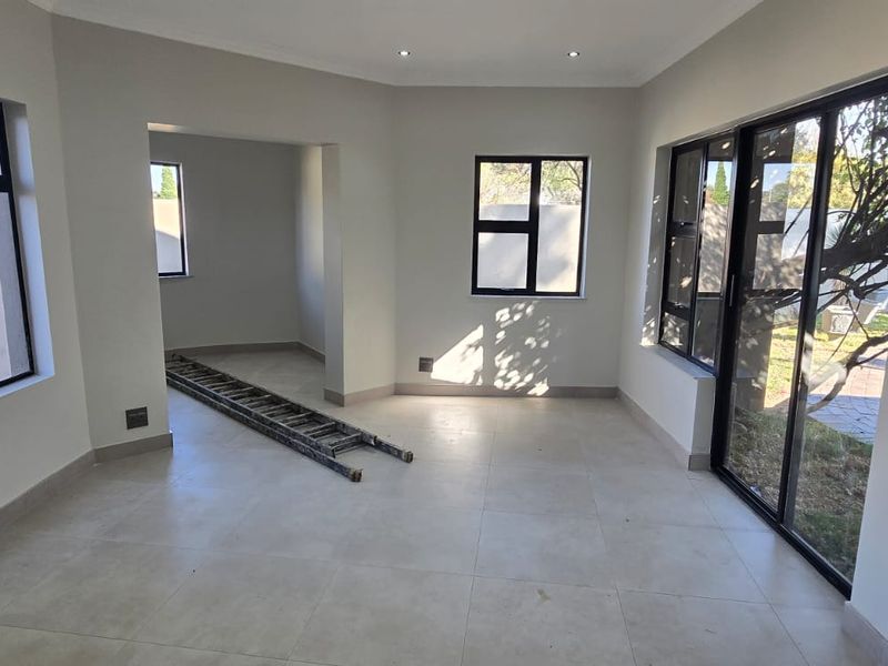A bright, empty living area featuring neutral tiled flooring, modern aluminium-framed windows, and a sliding glass door providing access to the garden.