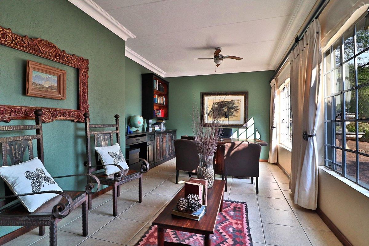 A spacious living area featuring tiled flooring, crown molding, a ceiling fan, and large windows that provide ample natural light.