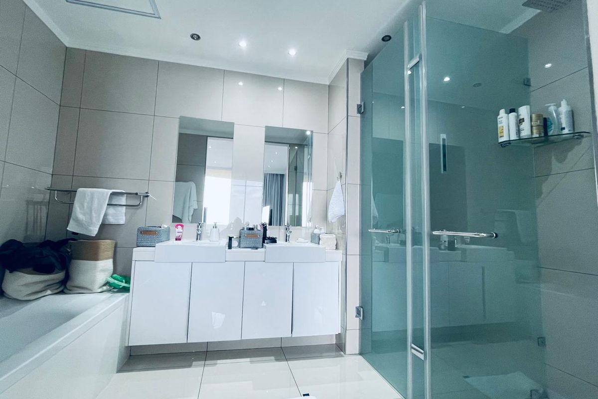 Modern bathroom featuring a double vanity, glass-enclosed shower, and a built-in bathtub with neutral floor-to-ceiling tiling and recessed lighting.