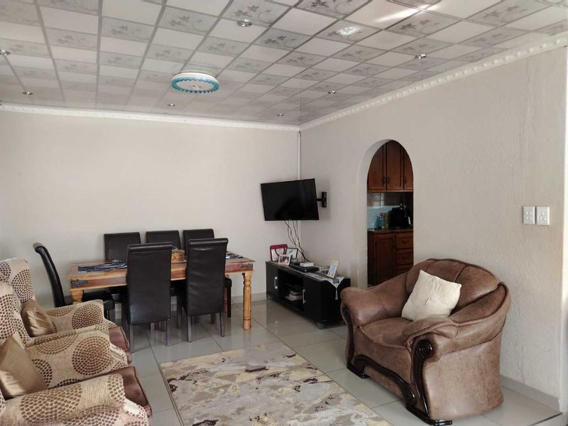Open plan living and dining area featuring tiled floors, an arched entryway to the kitchen, and decorative ceiling panels.