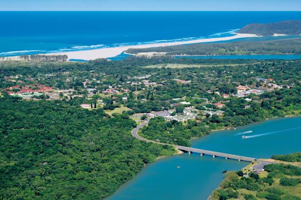 An aerial view of the coastal landscape, featuring a river, bridge, and surrounding lush vegetation leading to the ocean.