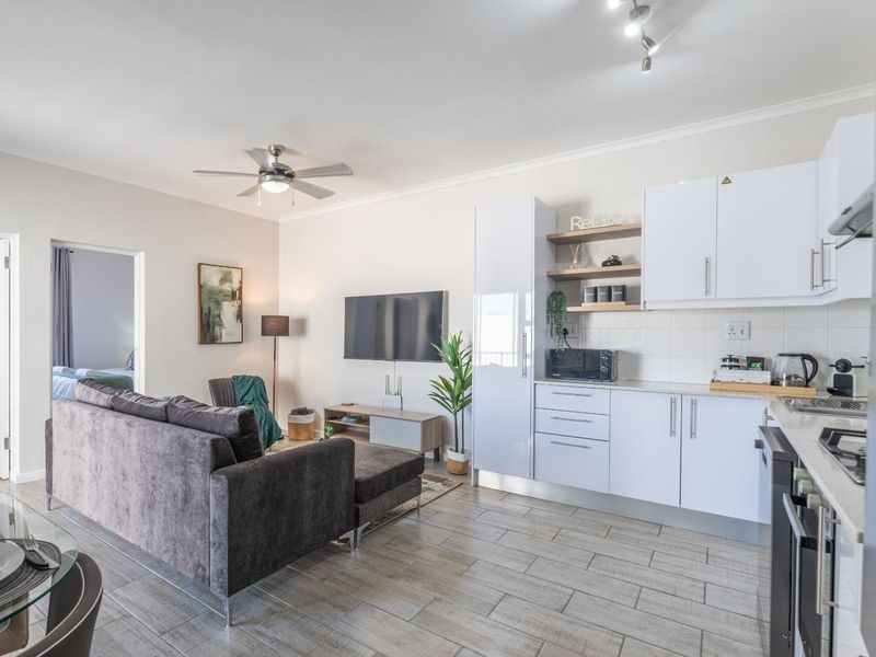 Modern open-plan living area featuring a contemporary kitchen with white cabinetry, gas hob, and tiled flooring, seamlessly flowing into the lounge space.