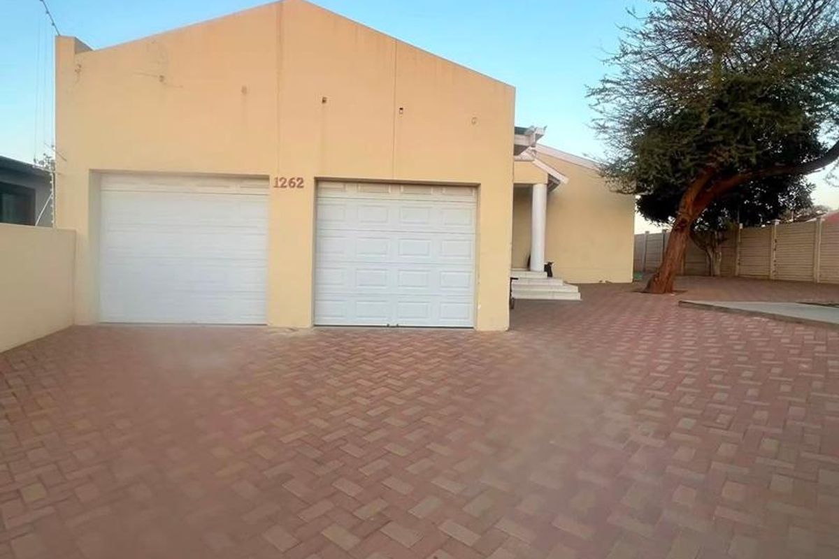 Front view of the property featuring a double garage with sectional doors and a spacious paved driveway.