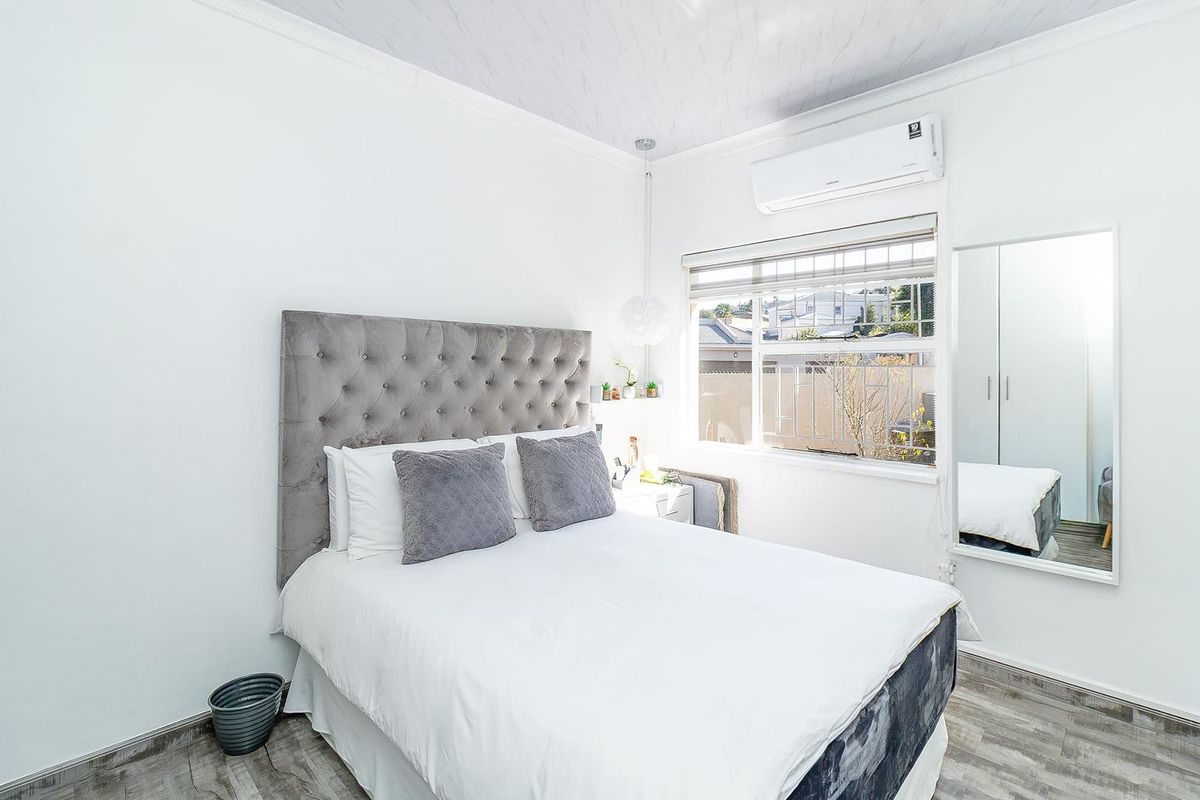 A well-maintained bedroom featuring laminate flooring, a split-system air conditioner, and a built-in wardrobe with a full-length mirror.