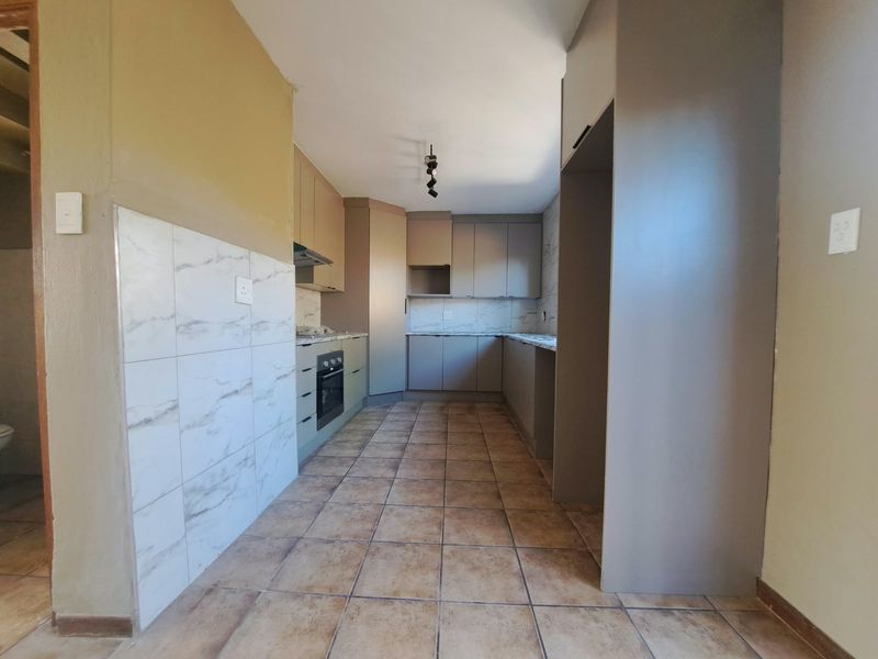 A functional, empty kitchen featuring built-in cabinetry, integrated oven and hob, tiled splashbacks, and tiled flooring, offering a blank canvas for updates.