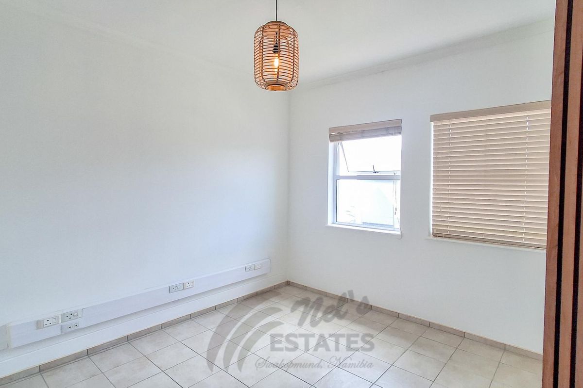A bright, empty bedroom featuring tiled flooring, neutral walls, and fitted window blinds, suitable for use as a bedroom or home office.