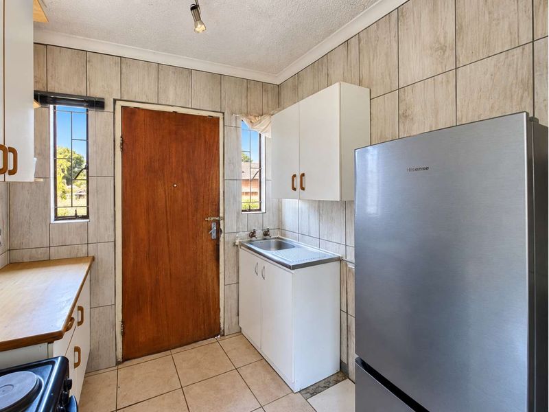 A functional scullery area featuring tiled walls, a stainless steel sink, built-in cabinetry, and direct exterior access through a wooden door.