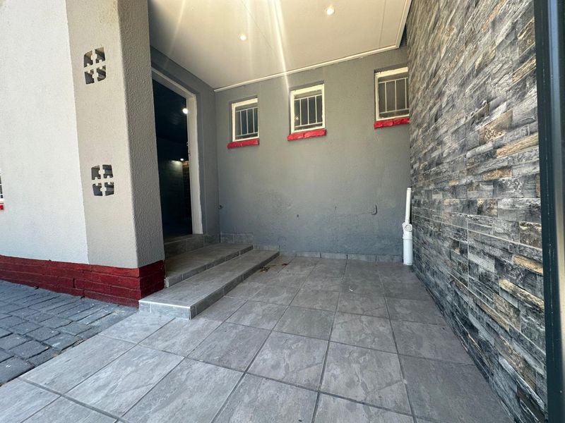 A covered patio area featuring tiled flooring, a stone-clad feature wall, and recessed ceiling lighting, providing a functional outdoor transition space.