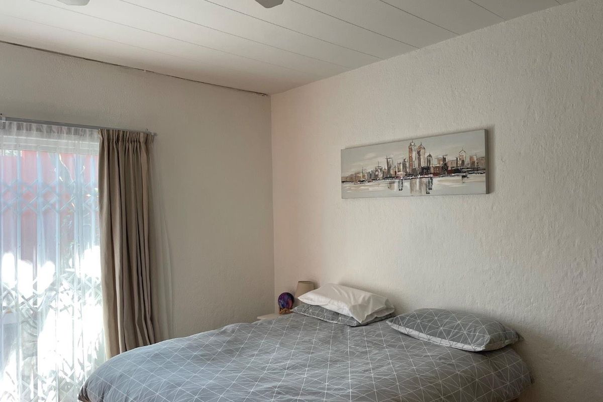 A bedroom featuring a ceiling fan, textured walls, and a sliding door with security gate access to the exterior.