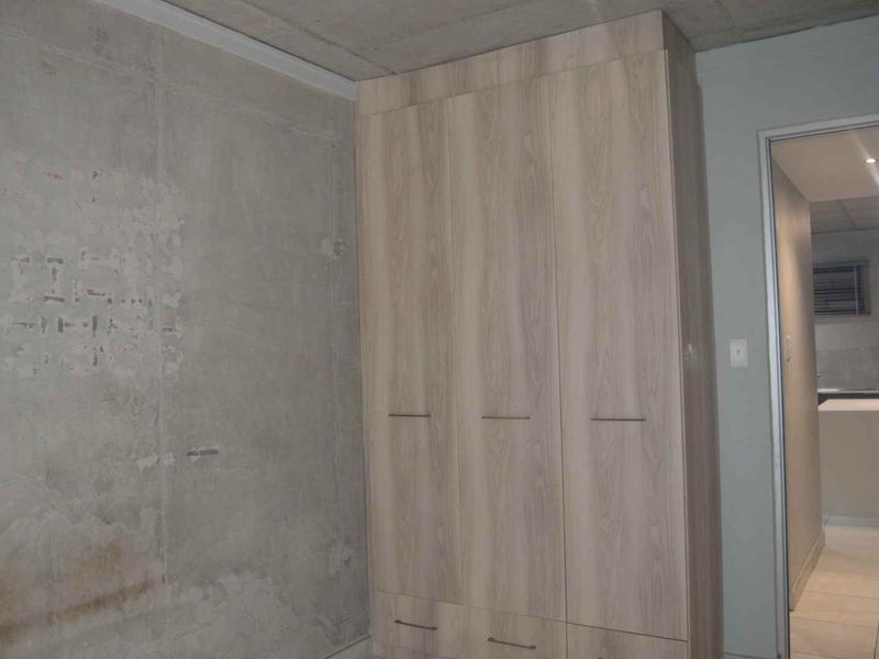 Bedroom featuring a built-in wardrobe and an unfinished exposed concrete wall, with an adjacent bathroom visible through the doorway.