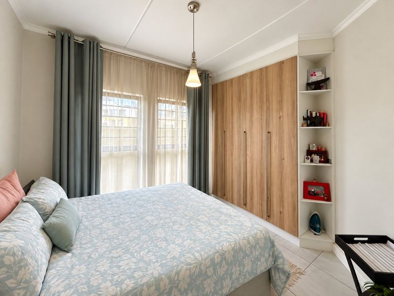 A well-maintained bedroom featuring modern wood-finish built-in wardrobes, integrated shelving, tiled flooring, and a pendant light fixture.