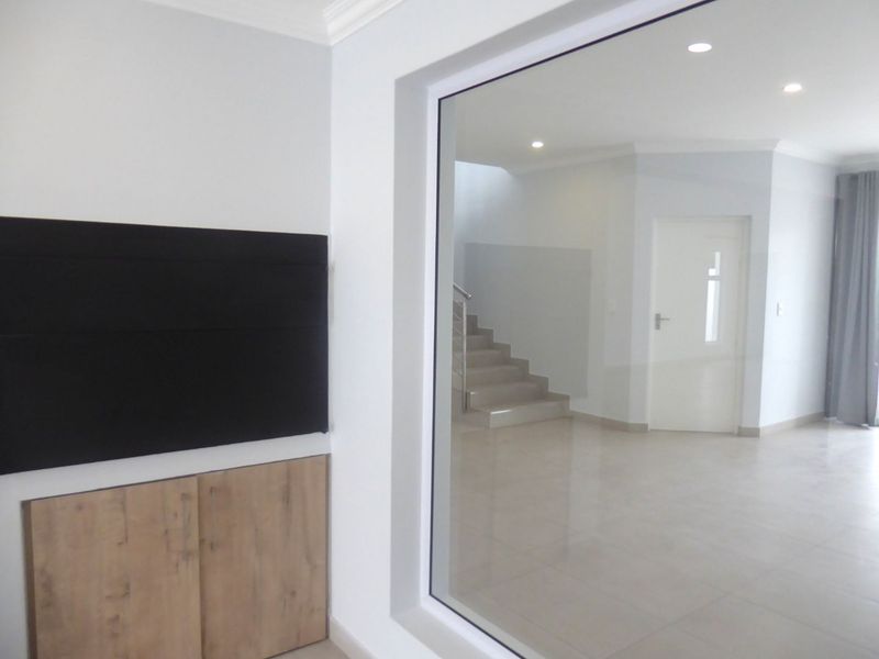A bright, modern living area featuring neutral tiled floors, recessed lighting, and built-in cabinetry, with a clear view of the internal staircase.