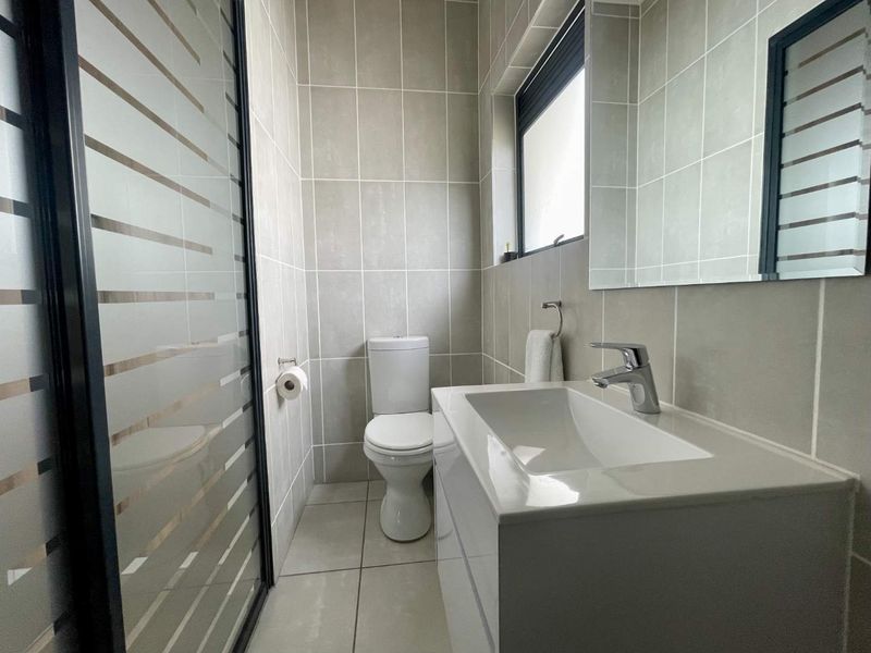 A modern, well-maintained bathroom featuring neutral wall and floor tiles, a sleek vanity with basin, and a frosted glass shower enclosure.