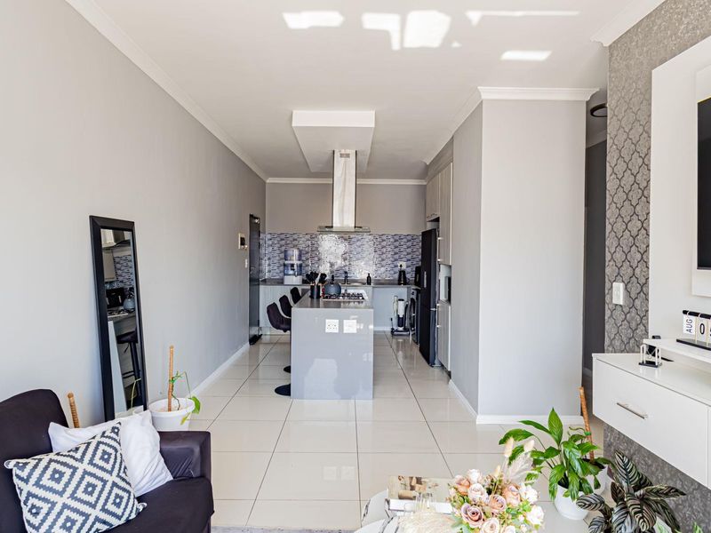 Modern open-plan living area featuring a sleek kitchen with a central island, extractor fan, and contemporary tiled flooring throughout.