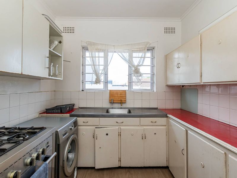 A dated kitchen featuring original cabinetry, a stainless steel sink, tiled backsplash, and a gas stove, offering significant potential for modernization and renovation.