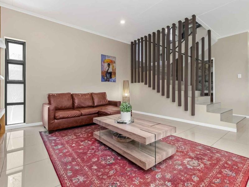Modern living room featuring polished tiled floors, a striking vertical timber slat staircase balustrade, and neutral wall tones.