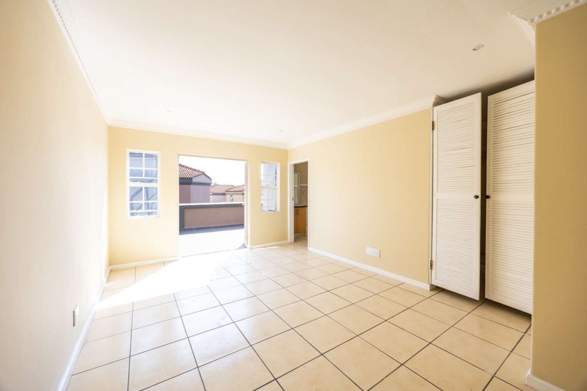 A bright, empty bedroom featuring tiled flooring, built-in cupboards with louvered doors, and direct access to an outdoor balcony area.
