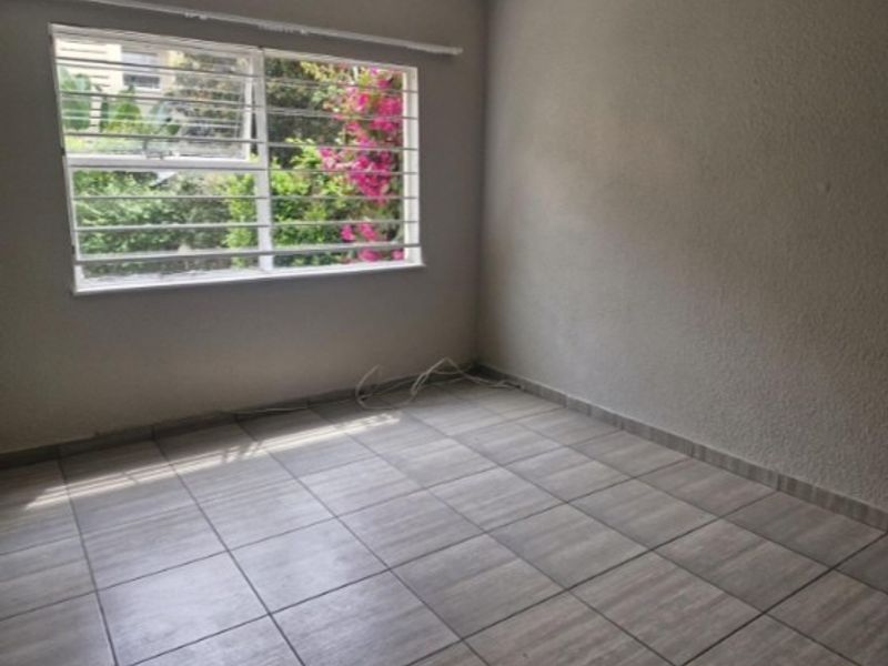 An empty bedroom featuring tiled flooring and a window fitted with security bars, offering a view of the garden.