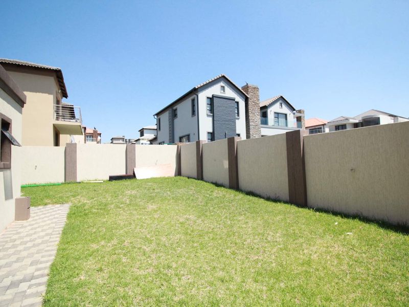 A private rear garden featuring a well-maintained lawn, paved walkway, and secure boundary walling.