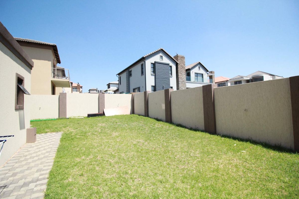 A private rear garden featuring a well-maintained lawn, paved walkway, and secure boundary walling.