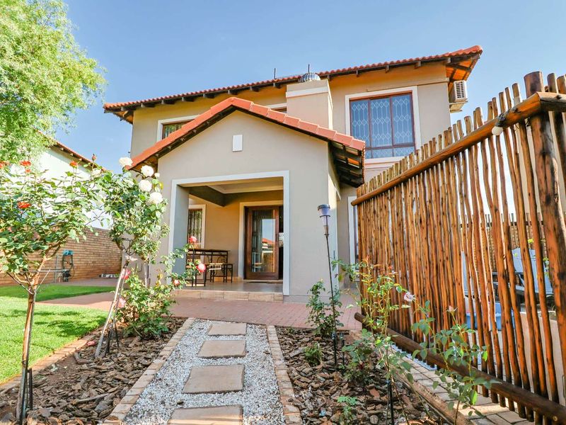 Rear view of the house featuring a covered patio, brick paved area, and a landscaped garden with a stone pathway.