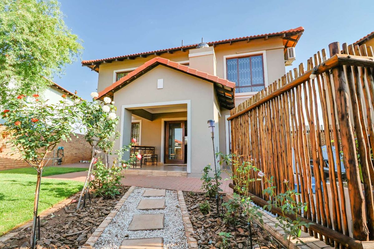 Rear view of the house featuring a covered patio, brick paved area, and a landscaped garden with a stone pathway.