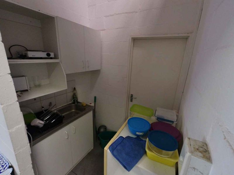 A compact industrial scullery area featuring a stainless steel sink, built-in cabinetry, and exposed blockwork walls, providing functional utility space.