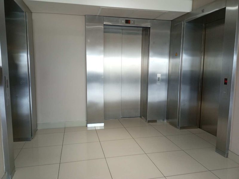 A clean and modern office building elevator lobby featuring stainless steel elevator doors and neutral tiled flooring.