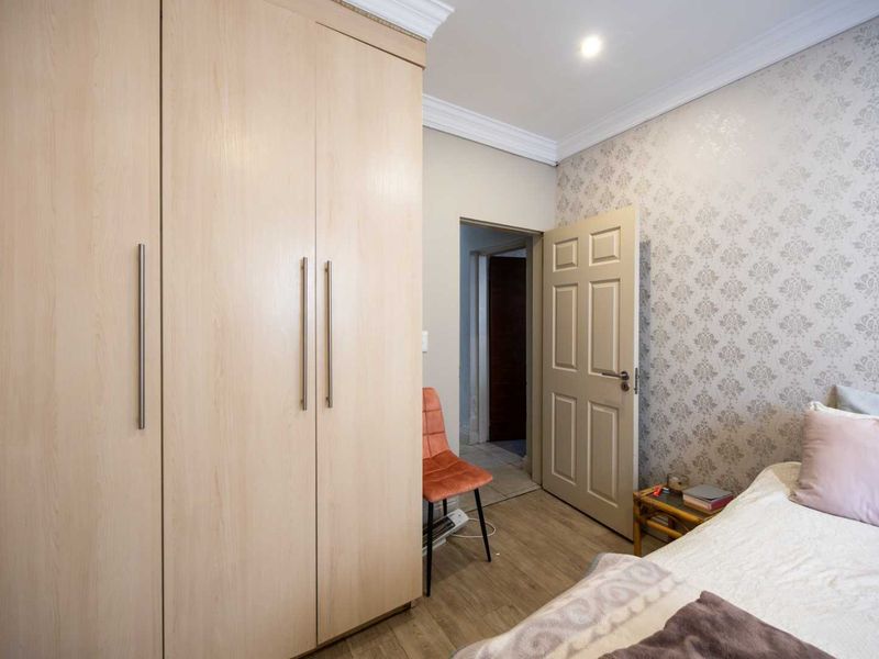A well-maintained bedroom featuring light wood-finish built-in wardrobes, decorative crown molding, and a feature wall with patterned wallpaper.