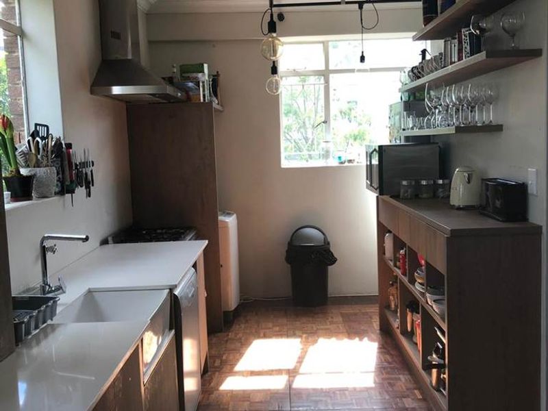 A functional kitchen featuring built-in cabinetry, floating shelving, a stainless steel extractor fan, and a sink with a modern countertop.
