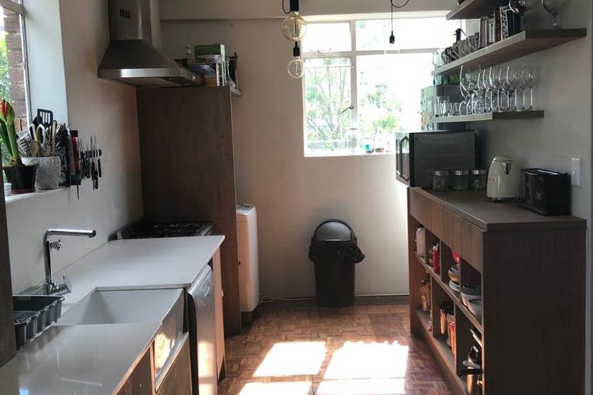 A functional kitchen featuring built-in cabinetry, floating shelving, a stainless steel extractor fan, and a sink with a modern countertop.