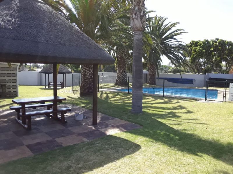 Communal outdoor area featuring a swimming pool, paved patio with a thatched lapa, and established garden surroundings.