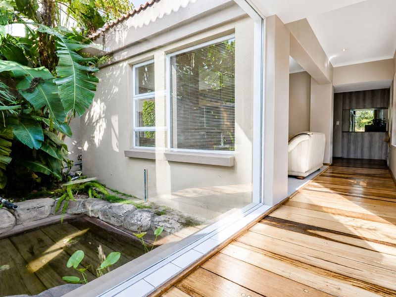 A bright, covered patio area featuring timber decking, a built-in stone-lined water feature, and large sliding glass doors connecting to the interior.
