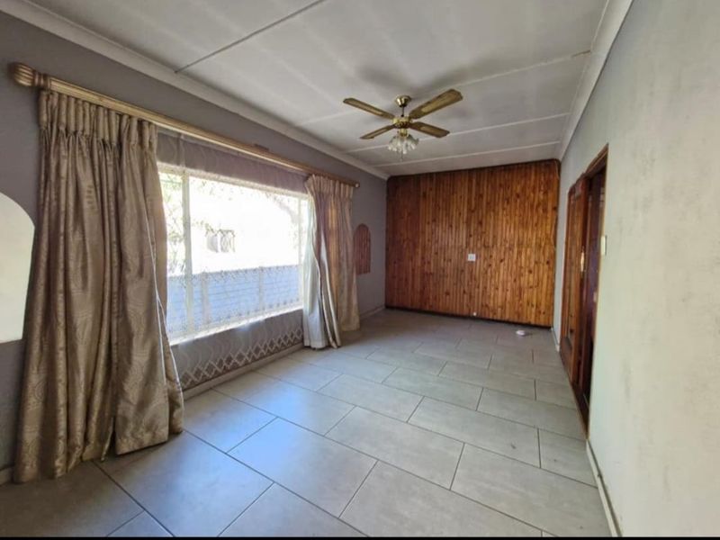 Spacious living room featuring tiled flooring, a wood-paneled feature wall, and a ceiling fan, offering a neutral canvas for potential updates.