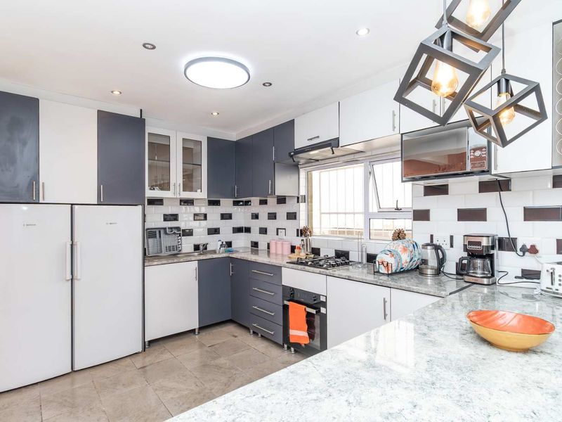 Modern kitchen featuring two-tone cabinetry, granite countertops, subway tile backsplash, and integrated appliances including a gas hob and oven.