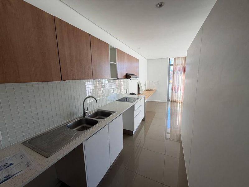 Modern galley-style kitchen featuring light wood-tone upper cabinets, white lower cabinetry, stone countertops, and integrated hob with extractor fan.