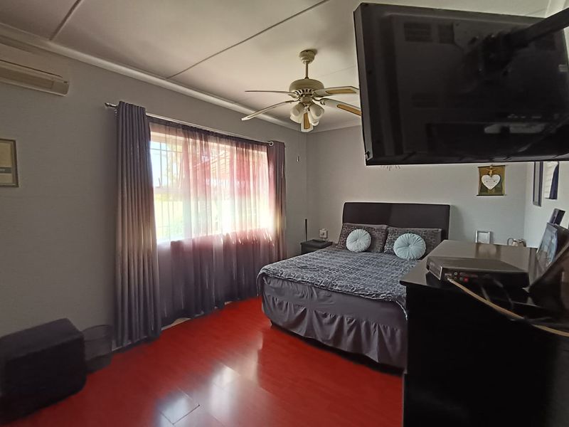 A bedroom featuring laminate flooring, a ceiling fan, and a wall-mounted air conditioning unit with security bars on the window.