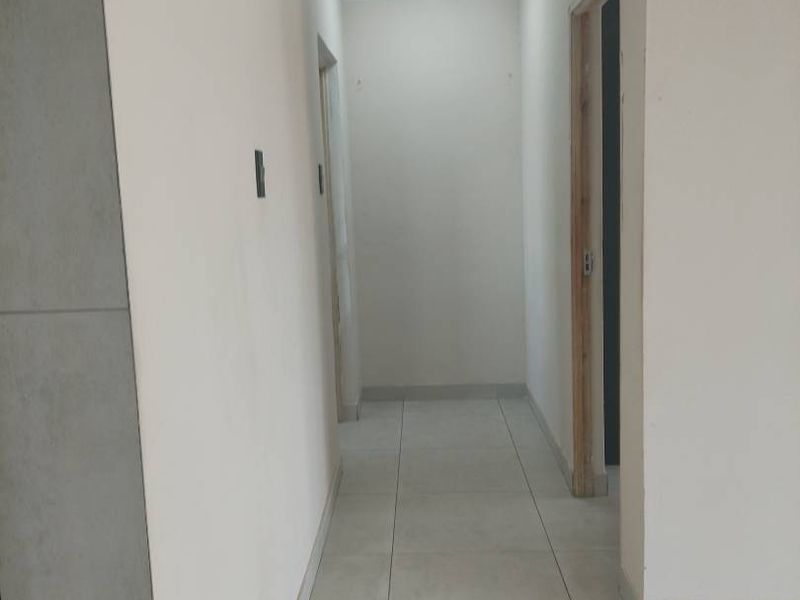 A vacant interior hallway featuring neutral tiled flooring and a recessed ceiling light, leading to adjacent rooms with unfinished door frames.