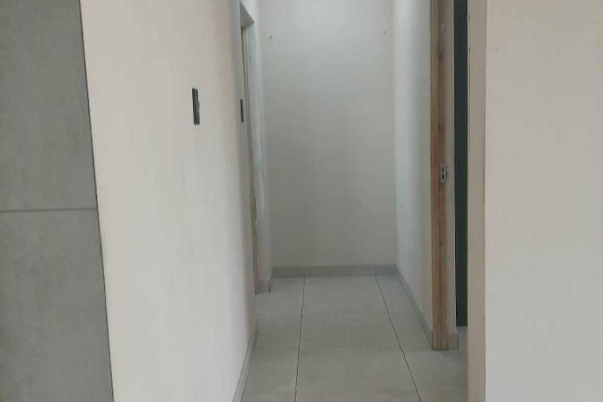 A vacant interior hallway featuring neutral tiled flooring and a recessed ceiling light, leading to adjacent rooms with unfinished door frames.