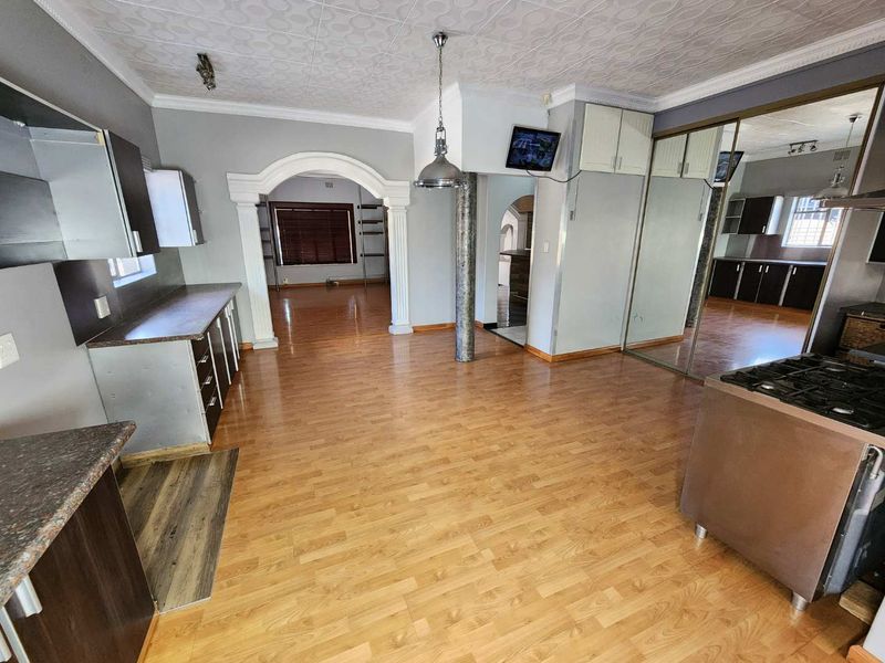 Spacious open-plan kitchen and living area featuring laminate flooring, decorative ceiling tiles, and extensive built-in cabinetry with mirrored storage.