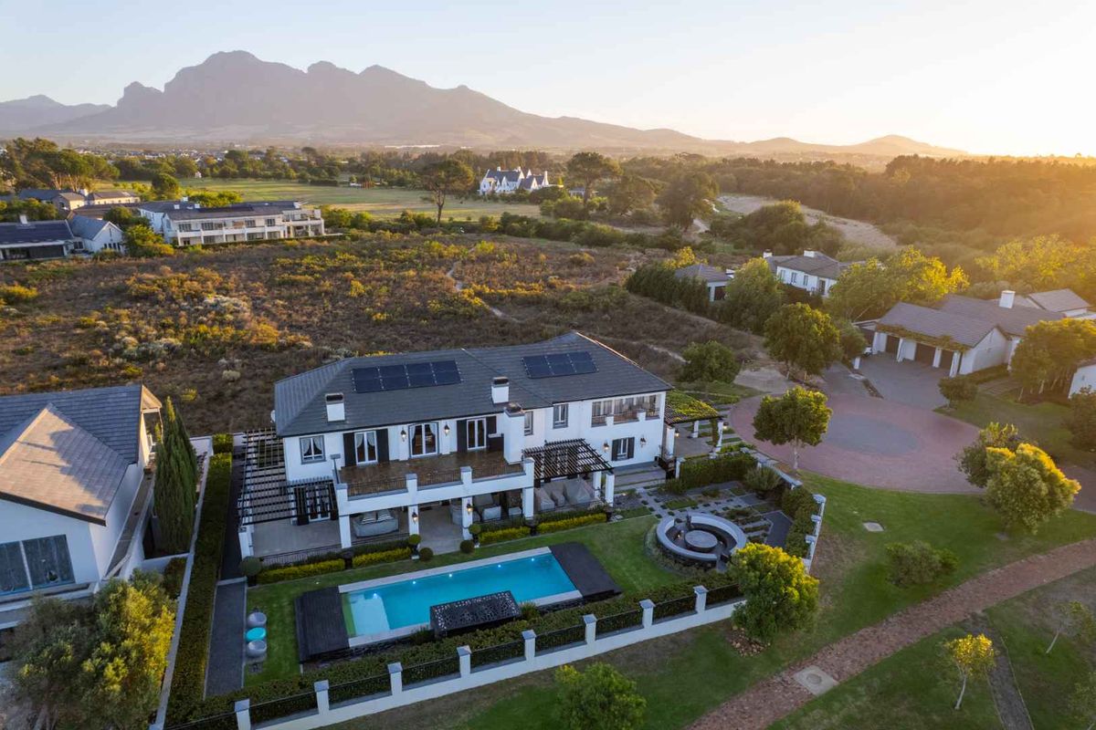 Aerial view of a luxury residence featuring a swimming pool, landscaped garden, solar panels, and scenic mountain views in a tranquil estate setting.