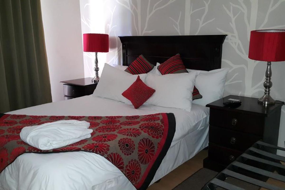 A well-maintained bedroom featuring a dark wood headboard, patterned wallpaper, and neutral flooring, providing a comfortable and functional guest accommodation space.