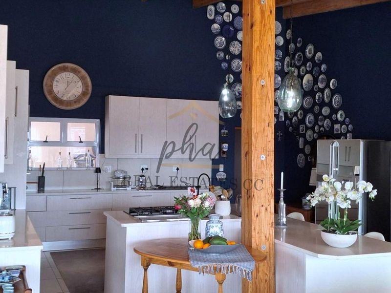 A spacious kitchen featuring light-toned cabinetry, a central island with a gas hob, and a striking dark blue feature wall with exposed timber elements.