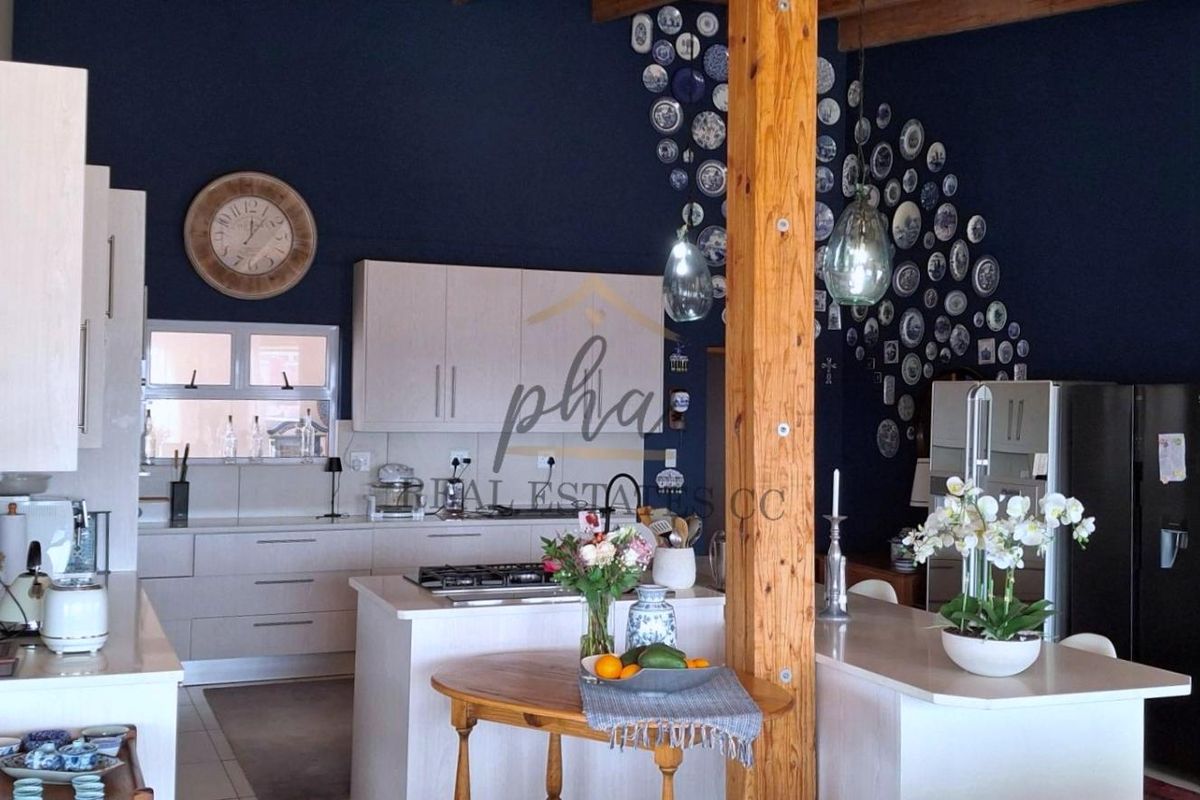 A spacious kitchen featuring light-toned cabinetry, a central island with a gas hob, and a striking dark blue feature wall with exposed timber elements.