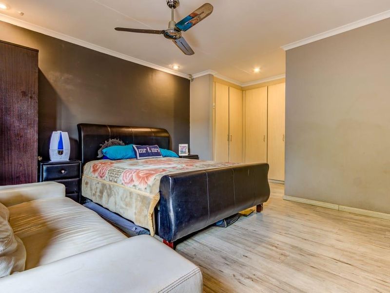 Spacious bedroom featuring laminate flooring, built-in cupboards, a ceiling fan, and recessed lighting, offering a functional layout with neutral wall finishes.