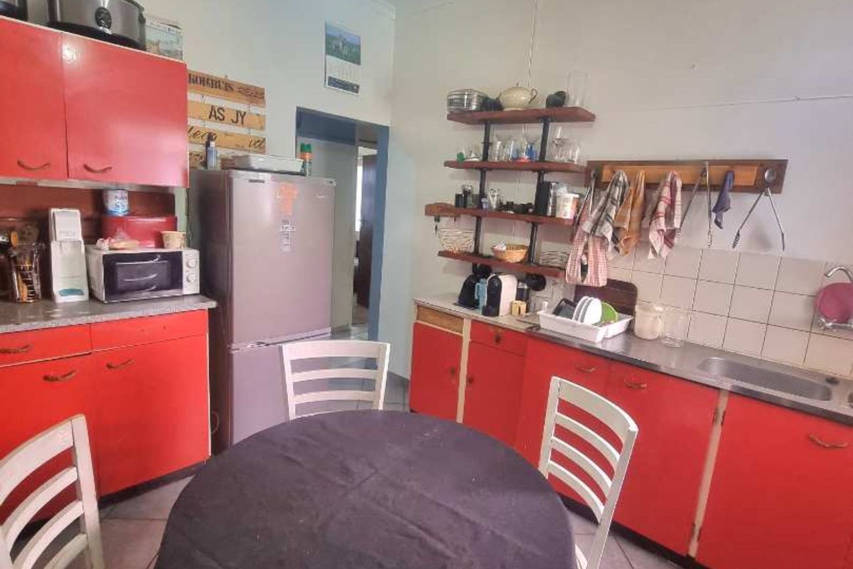A dated kitchen featuring red cabinetry, tiled flooring, and a stainless steel sink, offering a functional space with potential for modernization.
